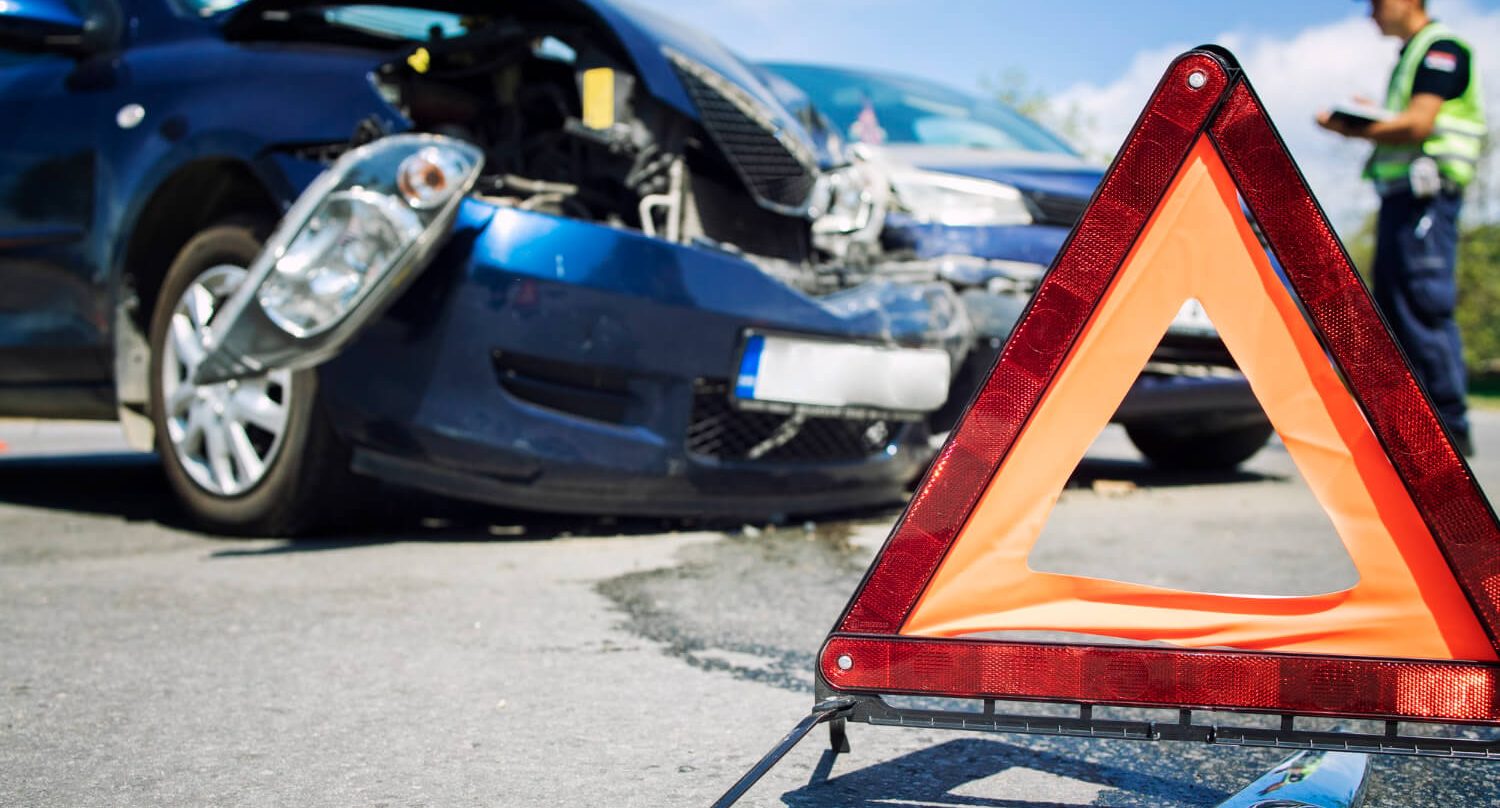 Pessoa parada perto de um acidente de automóvel com um triângulo a sinalizar