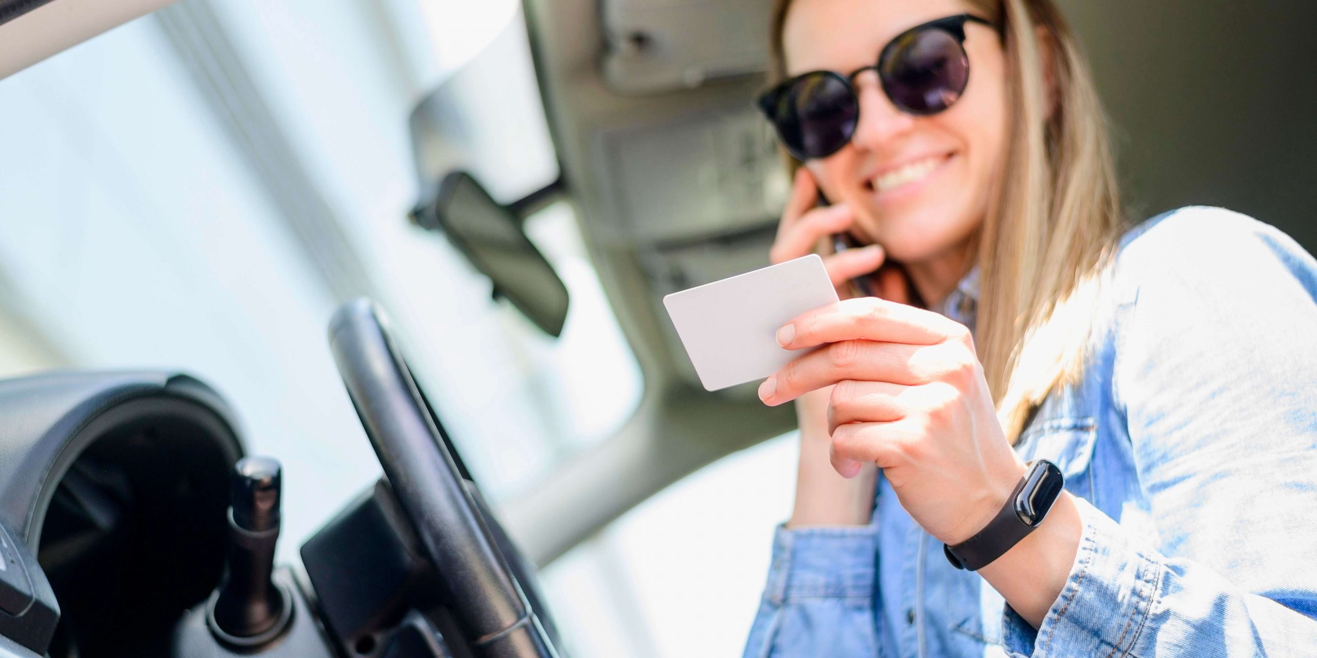 Mulher dentro de um carro segura a carta de condução enquanto fala ao telemóvel, representando o pedido da segunda via da carta de condução online.